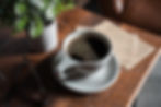 Fresh brewed coffee in a white coffee mug on a wooden table next to a plant and newspaper. 