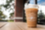 An iced latte in a Foxtail Coffee branded cold cup on a table outside.