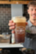A barista in a Foxtail Coffee uniform holding out a nitro cold brew in a plastic Foxtail branded to-go cup.